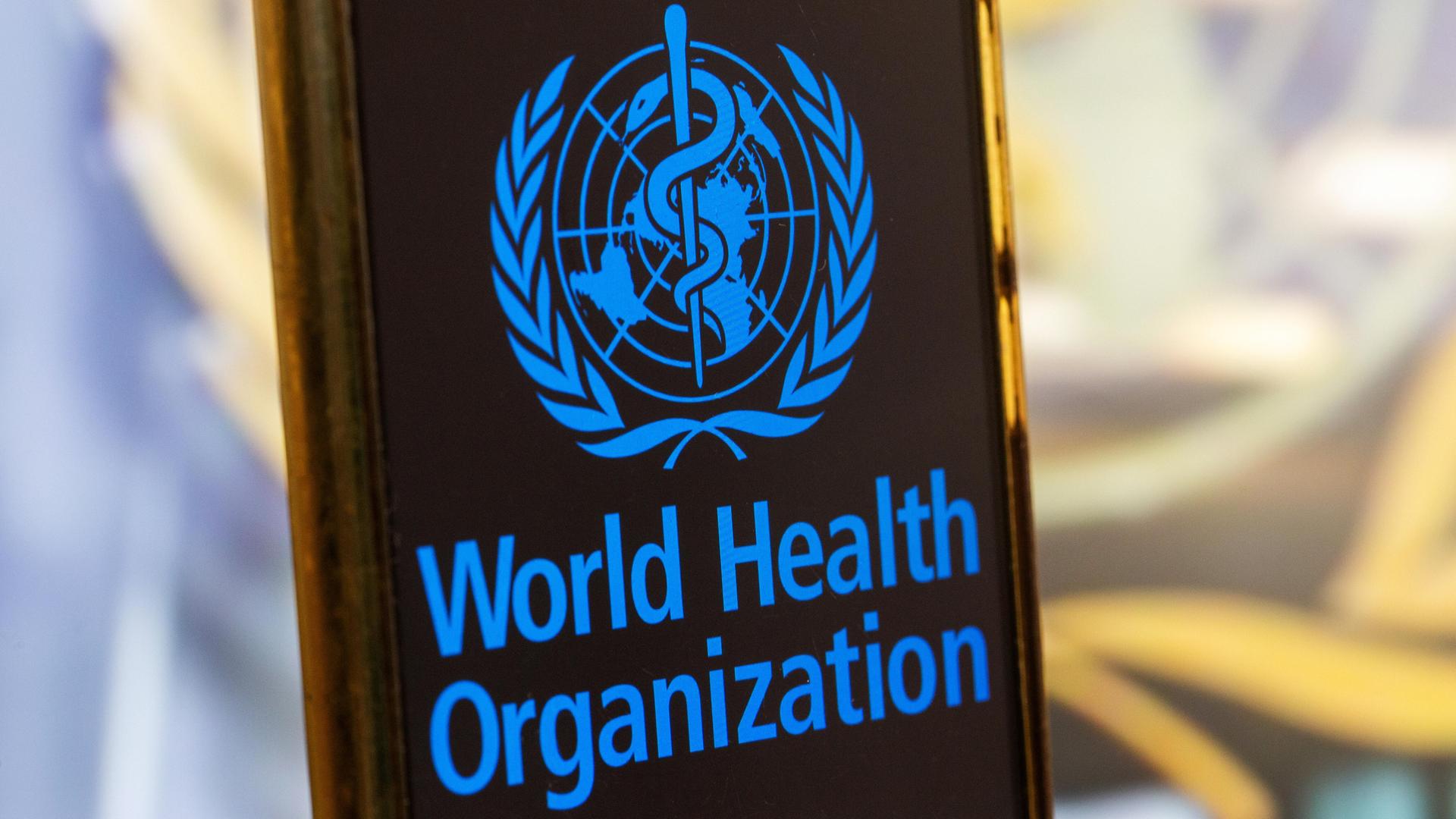 Symbolbild: Smartphone mit Logo der WHO (World Health Organisation) vor einem unscharfen Hintergrund