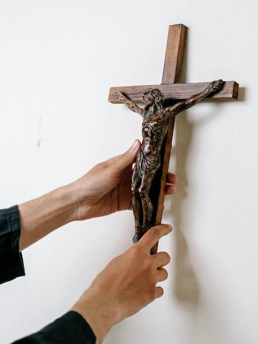 Ein Mann hängt ein Kruzifix an eine Wand.