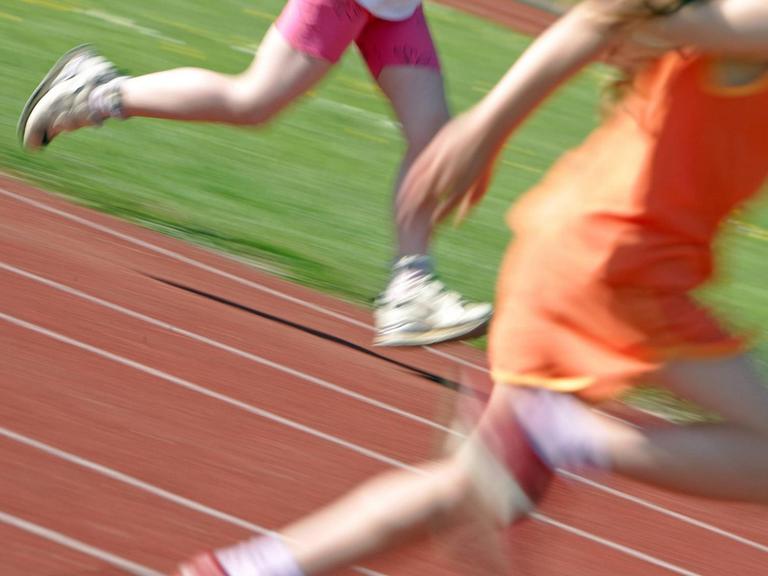 Kinder laufen über eine Laufbahn, zu sehen sind nur die Beine, unscharf.