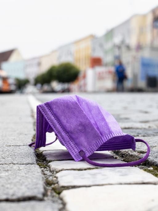 Eine violette medizinische Maske liegt auf einer Straße, während im Hintergrund die Altstadt von Mühldorf am Inn zu sehen ist. 