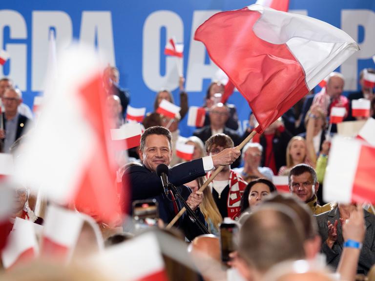 Rafał Trzaskowski schwenkt die polnische Flagge. Die Szene spielt sich am Sonntagabend, dem 18. Mai 2025, in Sandomierz ab. Im Hintergrund jubeln Unterstützer, viele halten kleine und große Polenfahnen in die Höhe. 